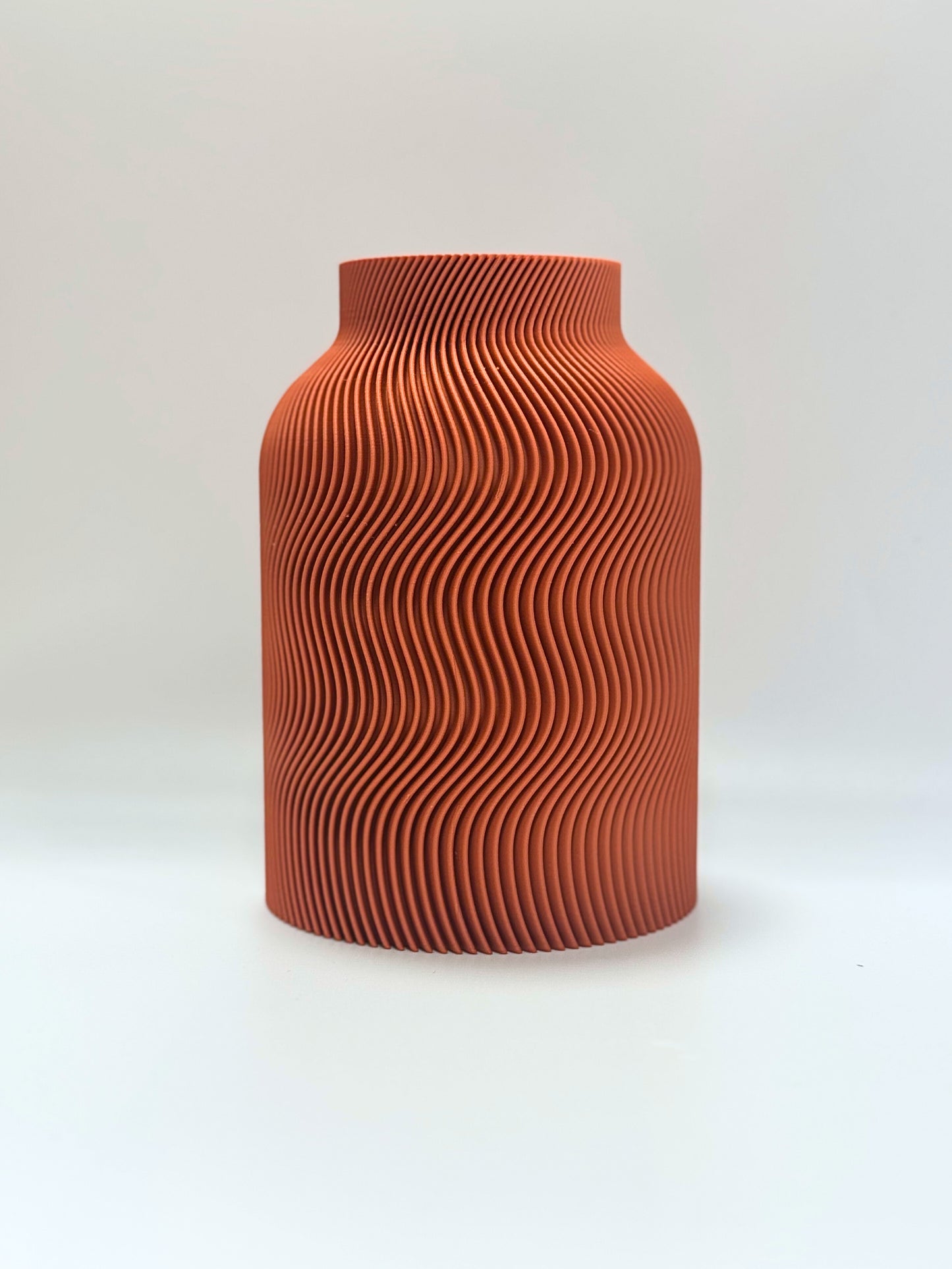 Terracotta-colored vase with wavy pattern on a white background