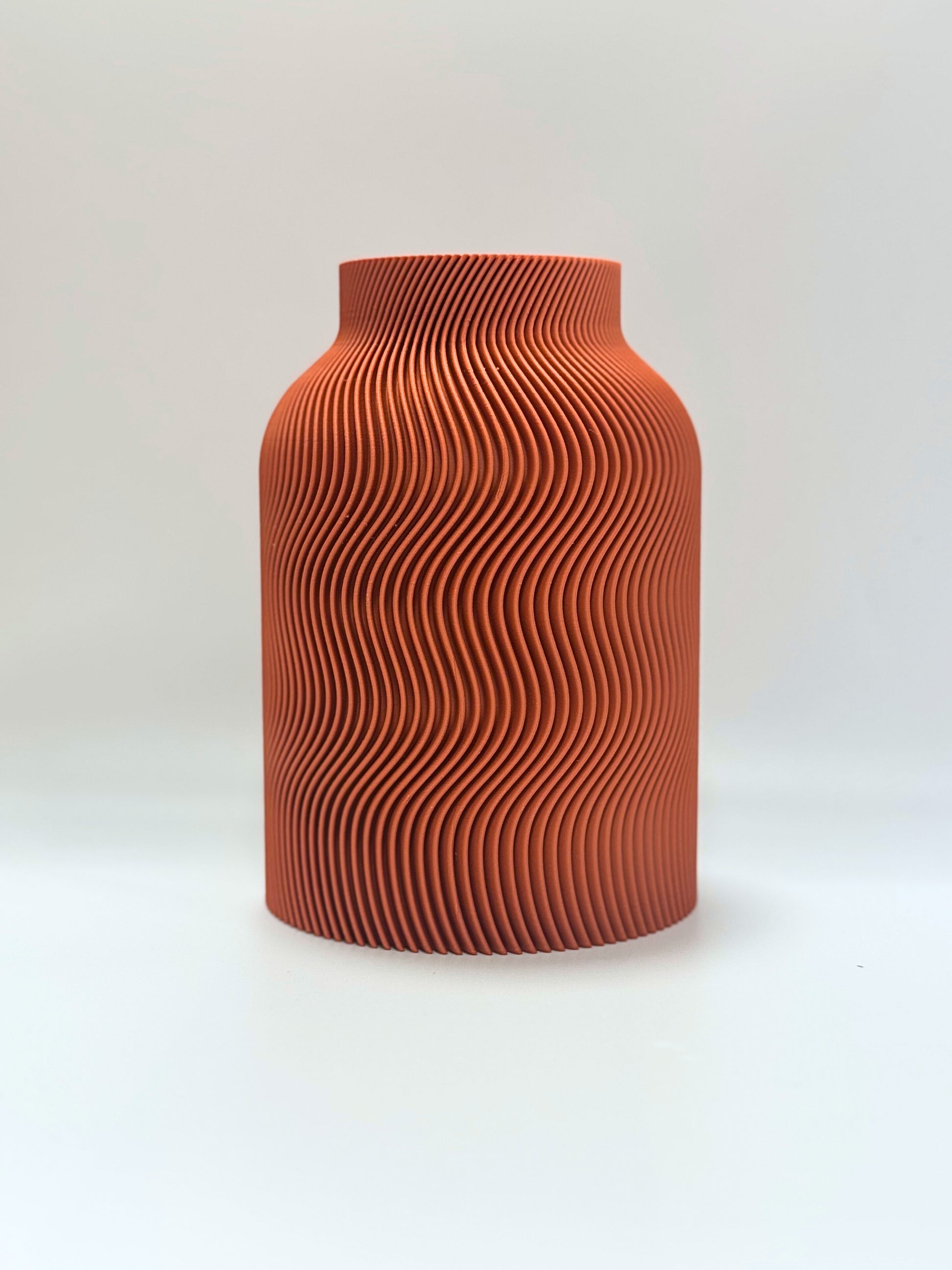 Terracotta-colored vase with wavy pattern on a white background
